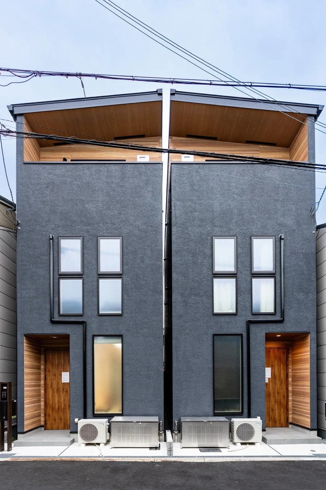 Exterior of the neighbouring three-storey houses, with dark walls and timber entrances